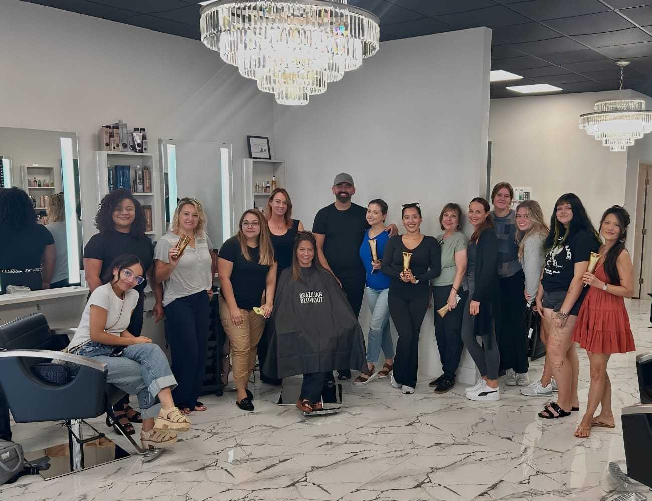 Group of people smiling in a salon, holding glasses, under modern chandeliers.