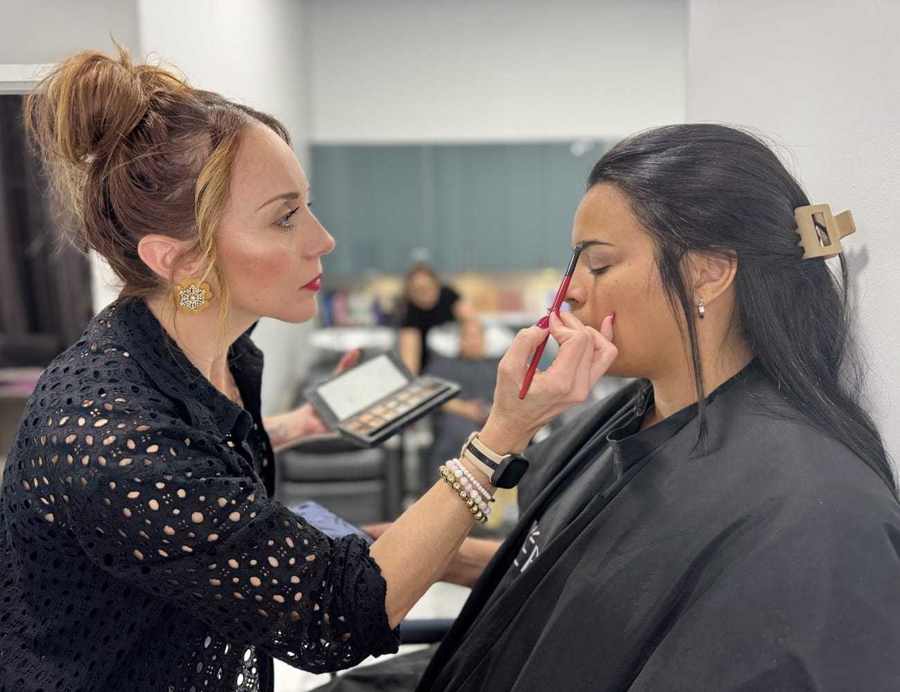 Makeup artist applying eyeshadow to a woman in a salon.