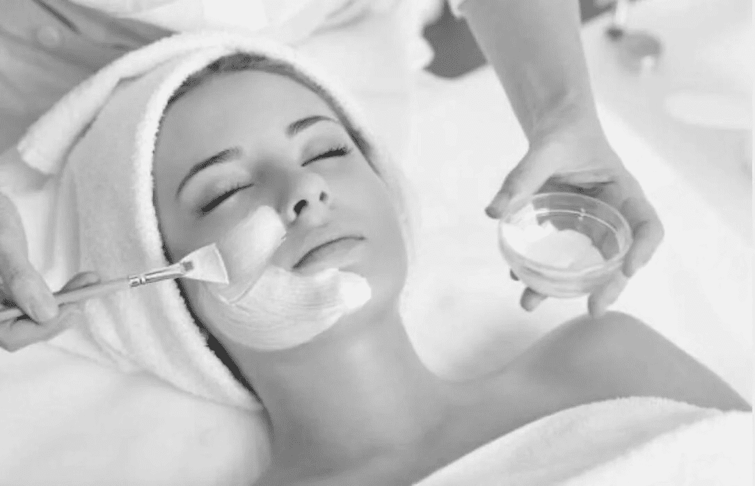 Facial treatment with a brush and mask applied to a relaxed woman in a spa setting.