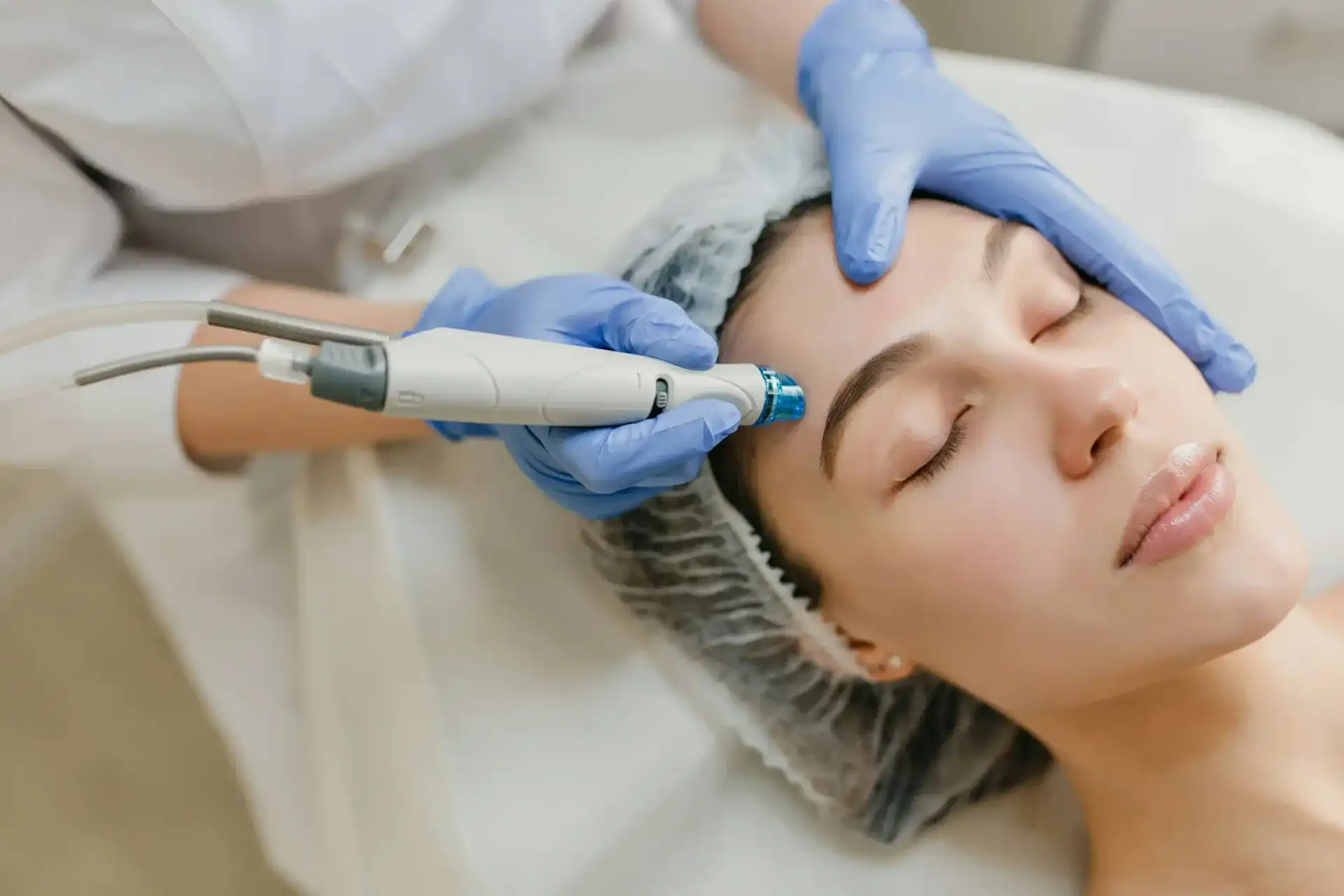 A woman receives a facial treatment from a professional using a specialized device.