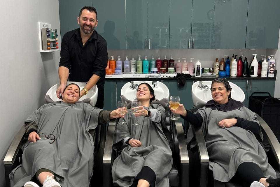Group enjoying salon hair wash while sipping drinks, smiling at the camera.